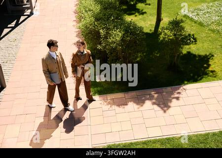 Young man and woman walk side by side, engaged in thoughtful conversation under bright sunshine. Stock Photo