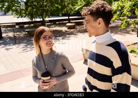 Two young coworkers share a light hearted moment while strolling outside, surrounded by greenery. Stock Photo