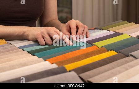 Hands choose fabric swatches from an upholstery selection. Colorful textile strips cover the surface. Stock Photo