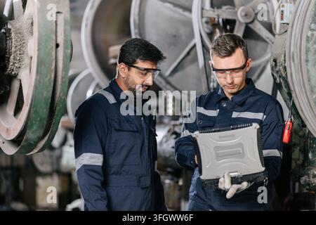 Engineers Monitor Machine Operation Using Laptop in Heavy Industry Factory in India. Professional Engineer workers working at computer service machine Stock Photo
