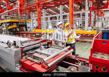 Technician Team Inspecting Production Line Steel Roll Forming Machine, Senior Engineer Workers Men Working Together In Metal Sheet Plant Factory Stock Photo