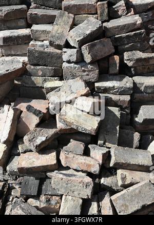 Aged brick pile showing weathered variegated red brick surfaces with soot stains, engraved bricks, and wood chips Stock Photo