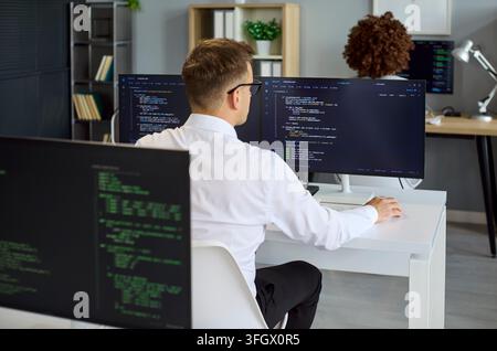 Rear view of developer coding at dual monitors in contemporary tech office Stock Photo