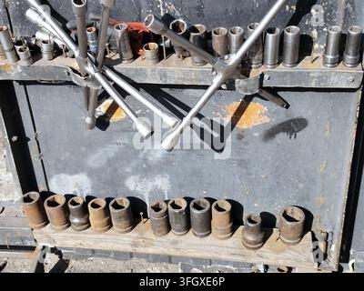 Set of metal socket wrenches and assorted sockets arranged on a weathered tool rack, with strong sunlight creating shadows on the gray surface. Stock Photo