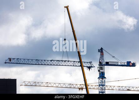 View of construction cranes operating against a cloudy sky in Vilnius, Vilnius County, Lithuania. Stock Photo