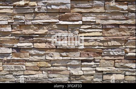 External wall coating made of stacked bricks of yellow, brown, beige and white stones. Panels for exterior. Background and texture. Stock Photo