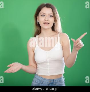 Young woman stands in front of green screen or chroma key background, talking while recording video or presentation Stock Photo