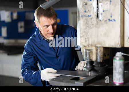 Concentrated experienced operator working on punching machine in industrial workshop, performing holes in metal workpiece Stock Photo