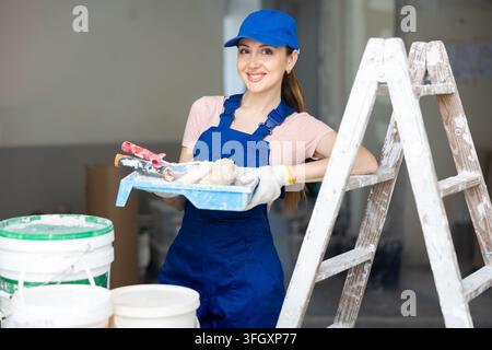 Portrait of young positive woman house painter holding tools posing in apartment under construction Stock Photo