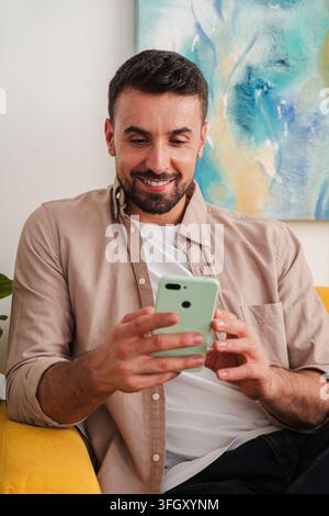 Candid shot of a man focused on a green smartphone, relaxed in a comfortable chair, enjoying a moment of digital interaction. Clean composition Stock Photo