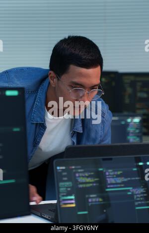 Focused young programmer analyzing source code and developing digital software with laptops, supporting programming, artificial intelligence, cybersec Stock Photo