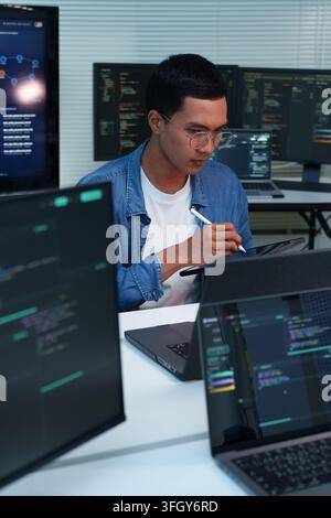 Focused programmer reviewing code and developing digital software, artificial intelligence, and cybersecurity solutions across multiple computer scree Stock Photo