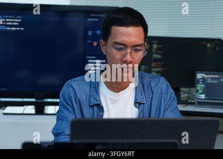 A focused young programmer works on a laptop, writing code and developing digital software solutions with expertise in programming, technology, and ar Stock Photo