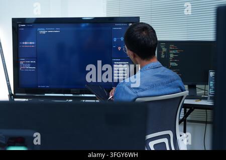A software developer works with digital code, programming tools, and artificial intelligence technology on multiple computer screens. Stock Photo