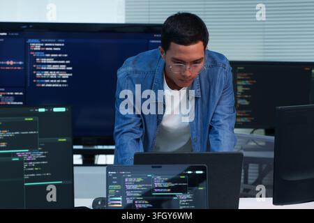 Focused programmer working on software development and writing code across multiple screens, representing digital technology, cybersecurity, artificia Stock Photo