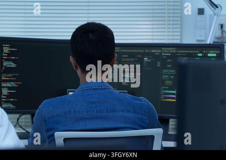 Back view of a programmer writing software code and developing artificial intelligence technology for digital and cyberspace applications. Stock Photo