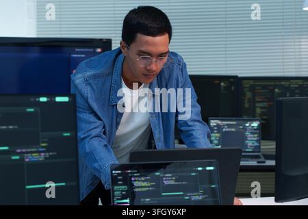 Focused programmer analyzing code and developing digital software solutions across multiple screens, representing modern technology, artificial intell Stock Photo
