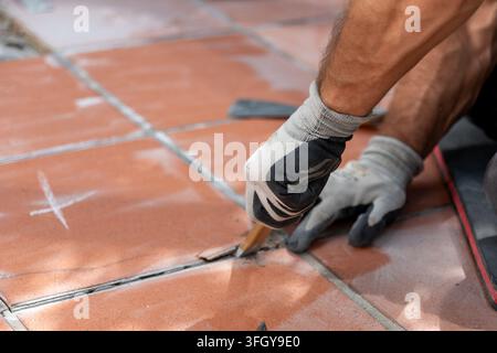 Worker in protective gloves pries up damaged floor tiles with a chisel during renovation work Stock Photo