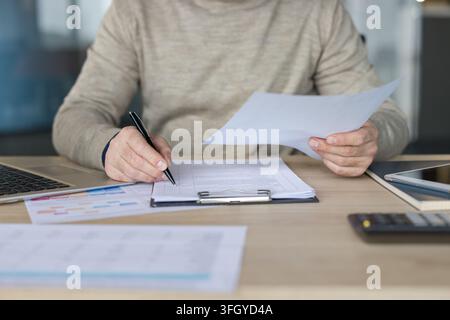 Businessman Writing On Documents At Desk In Office For Financial Analysis And Planning. Professional Manager Working With Laptop And Paperwork In Corporate Office Setting. Stock Photo