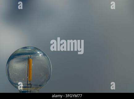 Close-up of a transparent LED filament bulb with yellow light strip against a soft gray background, leaving generous copy space for energy and lightin Stock Photo