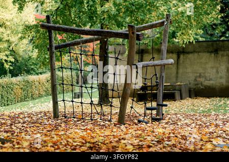 Wooden rope climbing frame stands on fallen leaves in an autumn playground. Concept of childhood, recreation, play, outdoor activity and movement Stock Photo
