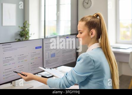 Professional woman analyzing AI dashboard on dual screens for business results Stock Photo