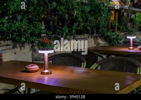 Close up of a wooden table with modern wireless metallic lamp and clay ashtray in open air cafe at night in Side. Stock Photo