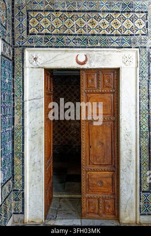 A white marble lintel doorway carved with an Islamic crescent emblem, surrounded by intricate hand-painted Qallaline ceramic mosaic wall tiles at the Stock Photo