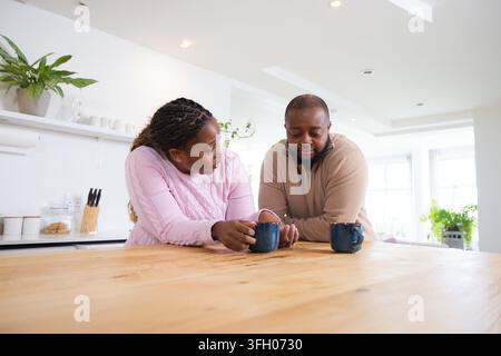 African American couple leaning on wood countertop holding dark blue mugs in bright kitchen Stock Photo