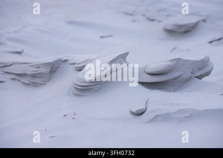 Wind-sculpted sand ridges are revealing layered overhangs on coastal dune, with scattered pebbles Stock Photo