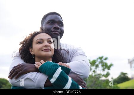 African American couple standing in park, man hugging woman wearing green white striped sweater Stock Photo