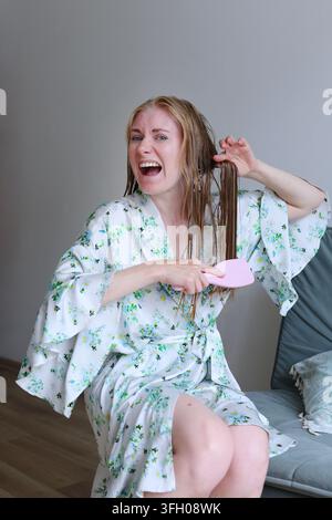 Frustrated woman pulling a brush through knotted hair, ideal for ads about conditioners, detanglers and repair treatments. Stock Photo