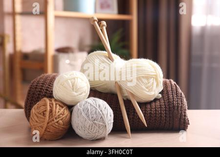 Skeins of yarns, sweater and knitting needles on wooden table indoors Stock Photo