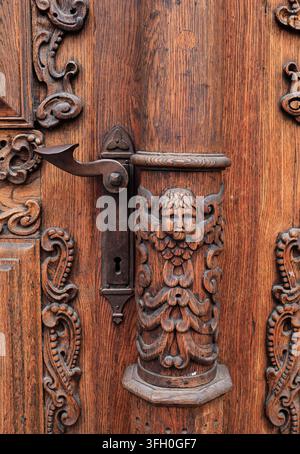 Tallinn, Estonia - Close-up of ornate carved wooden door with cherub figure relief, antique handle and keyhole Stock Photo