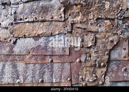 Old Riveted Metal Plates Texture - Close-up view of a rugged, weathered wall or surface made from overlapping, riveted metal plates with heavy rust an Stock Photo