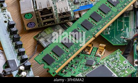 A pile of various electronic circuit boards, RAM memory module, and computer components lying on a wooden table. Concept for e-waste, hardware upgrade Stock Photo
