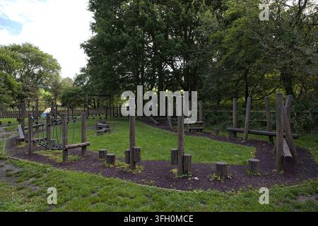 Wooden outdoor play area equipment and obstacle course set in a grassy clearing surrounded by trees. Stock Photo
