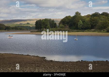Two small boats moored on the calm waters of Hollingworth Lake surrounded by trees and distant hills, Rochdale, UK. Stock Photo