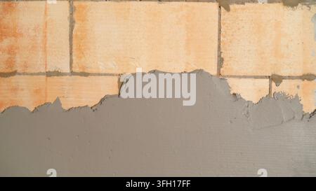 Close up shot of fresh grey plaster mortar being applied to a light brown aerated concrete block wall. Focus on texture of materials during renovation Stock Photo