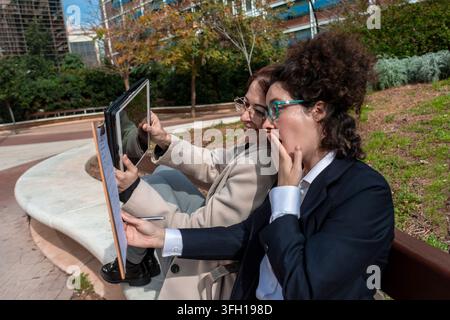 Businesswomen collaborating outdoors receiving surprising news on tablet Stock Photo