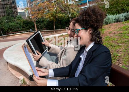 Businesswomen collaborating outdoors using tablet and clipboard Stock Photo