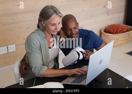 Couple sitting in home living area woman typing on silver laptop man holding white VR headset Stock Photo