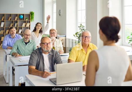 Adult students in computer training class, raising hands and engaging with teacher Stock Photo