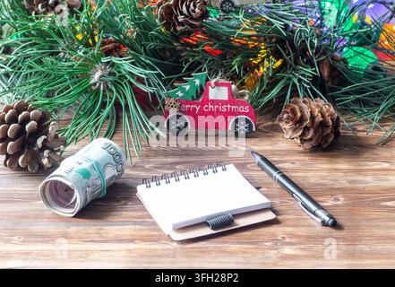 Rolled Russian ruble banknotes, a blank notebook, and a pen on a wooden table with Christmas decorations Stock Photo