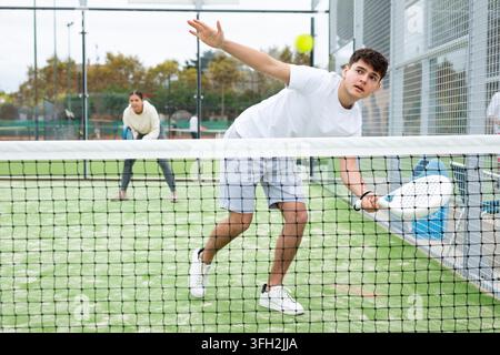 Sportive young man holding padel racquet in hand and ready to return ball while playing in court Stock Photo