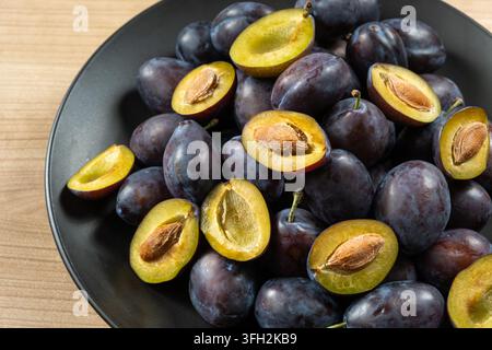 Fresh ripe plums and plum halves on black plate Stock Photo