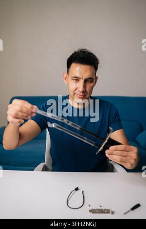 Vertical portrait of man assembling wi-fi module by connecting antennas sitting at white table in home office, focused on ensuring optimal performance Stock Photo