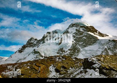 View of the snow-covered peaks of the Swiss Alps under a bright blue sky with wispy clouds in Zermatt, Valais, Switzerland. Stock Photo