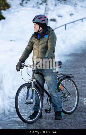 A senior man stands with his bicycle on an icy path in a snowy Helsinki park, Finland, enjoying healthy winter exercise. Stock Photo