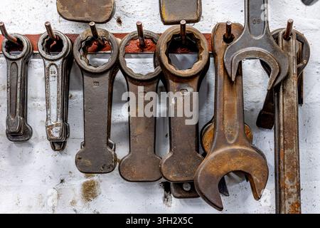 Rusty wrenches and various metal tools are neatly hanging on a wall rack in an industrial workshop, symbolizing repair, maintenance, and hard work in Stock Photo